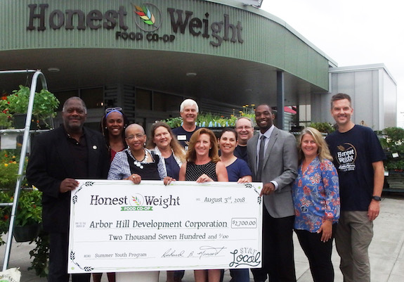 A group of people standing in front of Honest Weight holding a large check for $2,700 made out to Arbor Hill Development Corp from Honest Weight Food Co-op